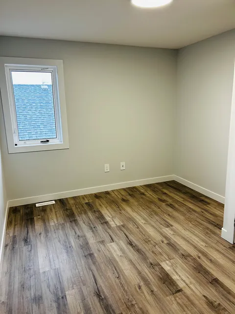 Empty room with a window, pale walls and wood-look flooring.
