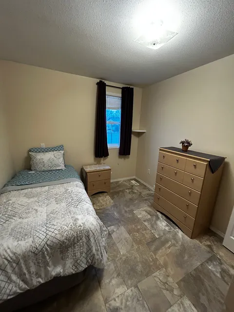 Bedroom with a single bed, wooden drawers, a window and a potted plant.