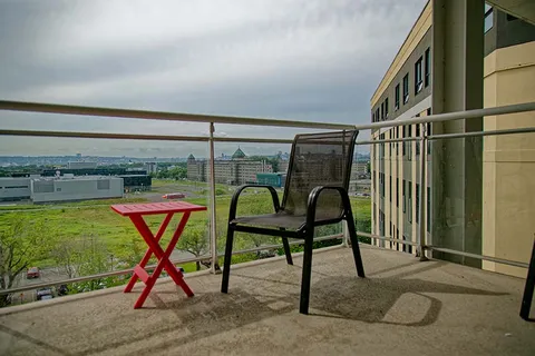 Balcony with a chair, red folding table and railing overlooking open ground