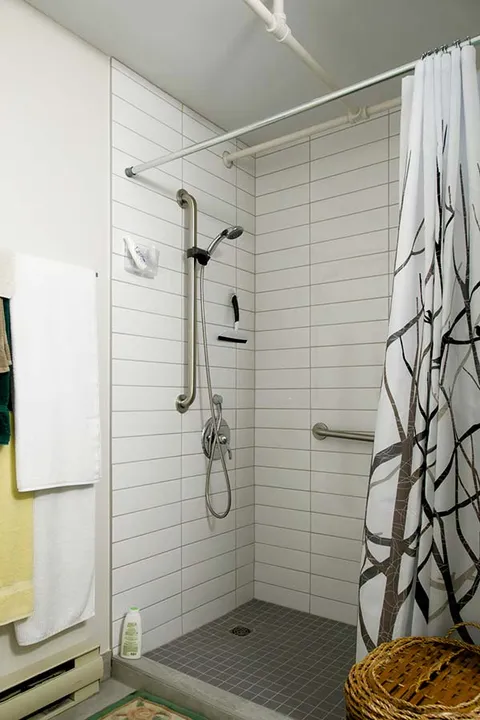 Tiled shower with grab bars, a handheld showerhead and a patterned curtain