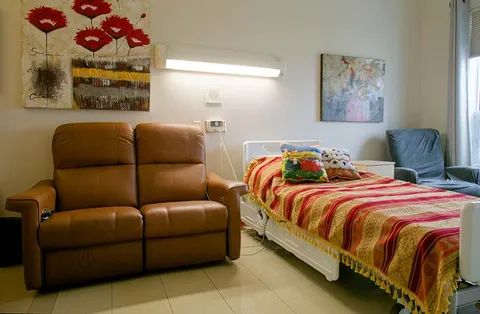 Bedroom with an adjustable bed, brown loveseat, blue chair and floral wall art