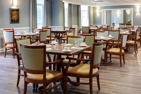 Dining room with wooden tables, upholstered chairs and large windows.