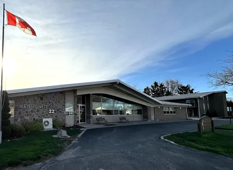 Residence entrance facade with a Canadian flag, benches and driveway.