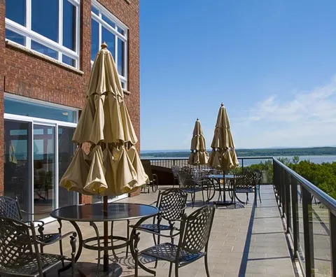 Terrace with metal tables, chairs, folded umbrellas and a water view