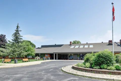 Single-storey brick building with a covered entrance, flagpole, benches and landscaped driveway