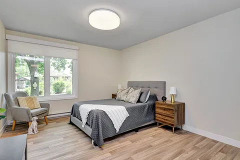 Bedroom with a grey bed, armchair, wooden bedside table and a window overlooking a gazebo