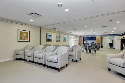 Room with rows of pale armchairs, framed owl and landscape pictures, tables and a kitchenette