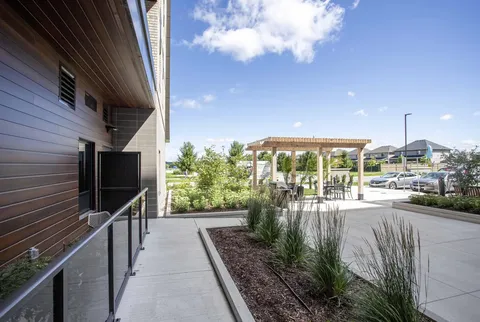 Paved path beside a residence wall leading towards a pergola