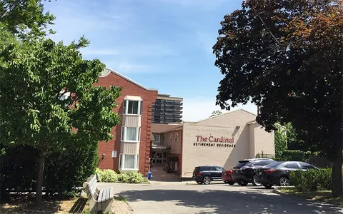 Brick building with an entrance courtyard, parked cars, a bench and leafy trees