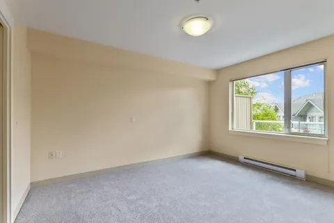 Empty carpeted room with a large window and pale walls