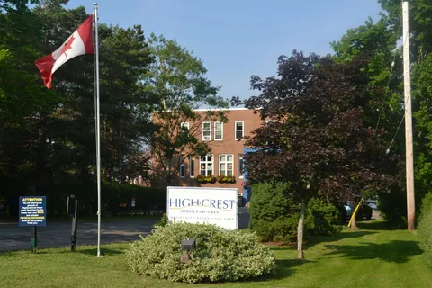 Brick building behind a lawn, trees, a Canadian flag and a residence sign