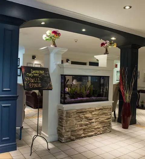 Aquarium on a stone-fronted base between white columns with flower arrangements