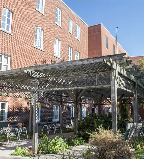 Brick building beside a patio with a pergola and planted beds