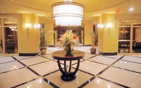 Lobby with a central flower arrangement, chandeliers and tiled floor.