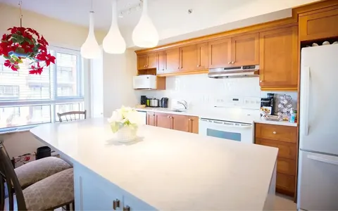 Suite kitchen with wood cabinets, white counters and pendant lighting.