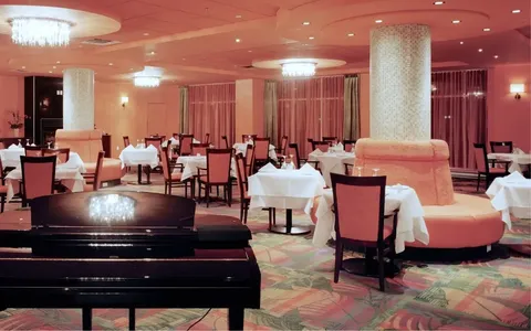 Dining room with set tables, upholstered chairs and a grand piano.