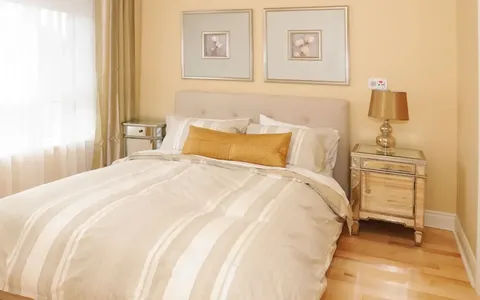 Bedroom with a double bed, mirrored bedside cabinets and gold cushions.