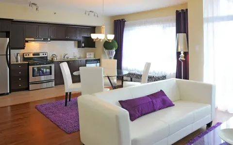 Open-plan suite with white sofa, kitchenette and purple rug.