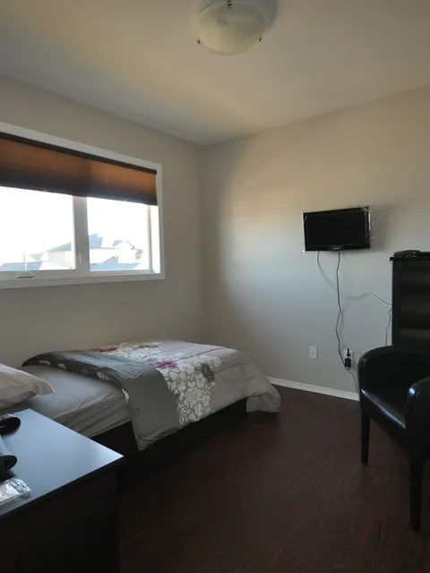 Bedroom with a single bed, armchair, dresser and wall-mounted television.