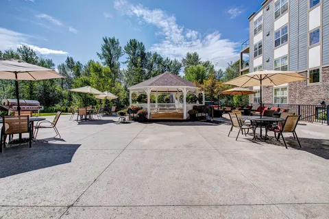 Paved patio with tables, umbrellas, a gazebo and landscaping.