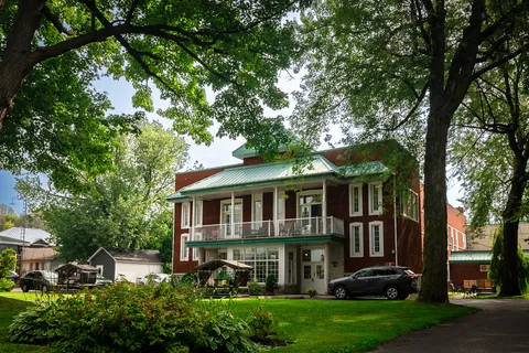 Brick residence with a green roof, covered upper balcony, lawn and mature trees.