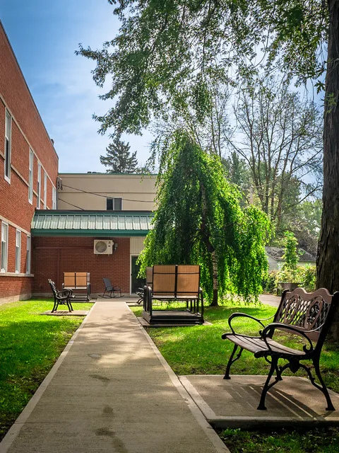 Garden path with benches, a swing and trees beside the brick residence.