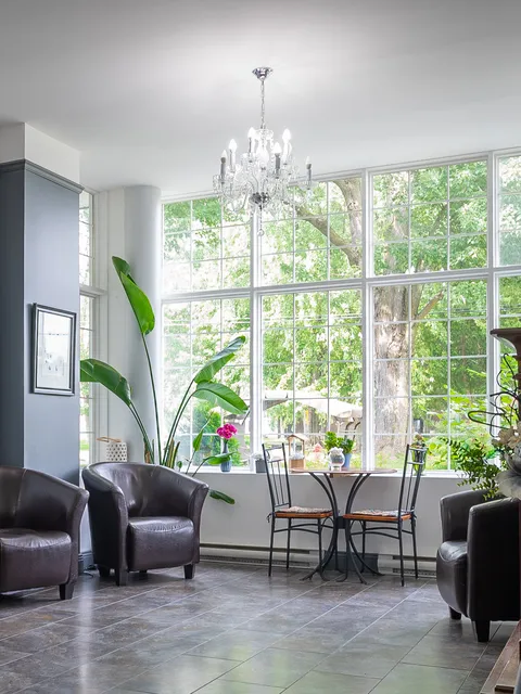 Sitting area with leather armchairs, a small table, chandelier and large garden-facing windows.