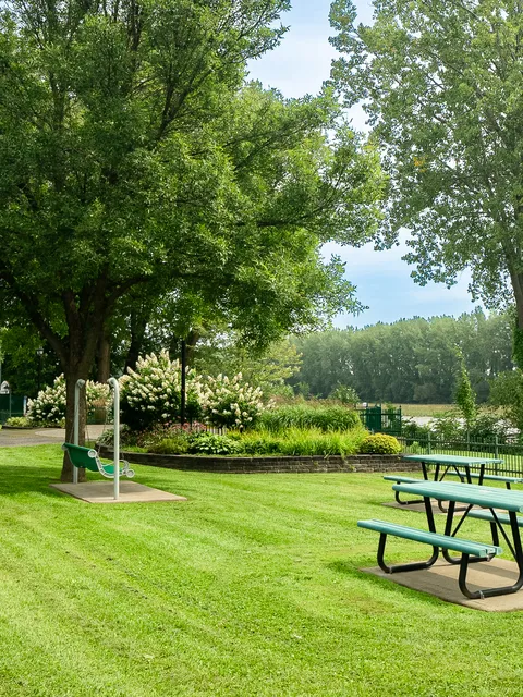 Riverside lawn with picnic tables, a garden swing, flower beds and mature trees.