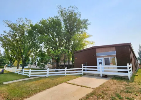 Brick residence entrance with a white fence, trees and a paved driveway