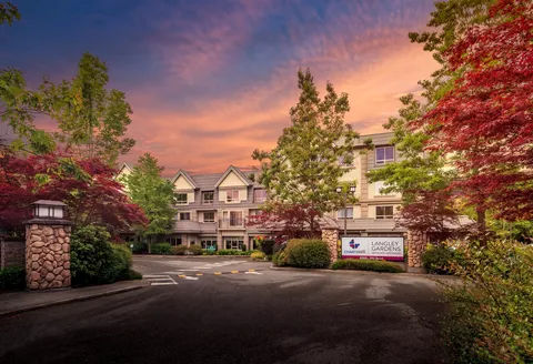 Residence building behind a driveway, shrubs and trees