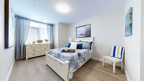 Bedroom with a white bed frame, blue patterned bedding, dresser and chair