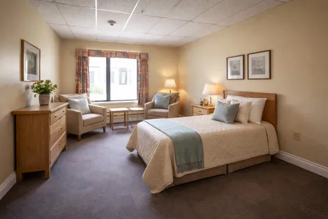 Bedroom with a bed, two armchairs, lamps and framed floral pictures