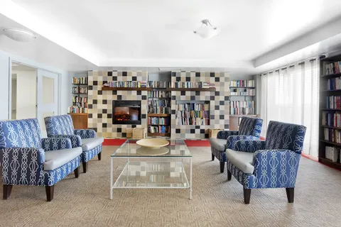Library with blue patterned armchairs, bookshelves, glass tables and a fireplace
