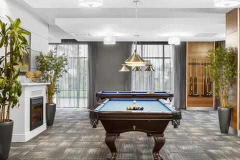 Two pool tables beneath hanging lights beside plants and a fireplace