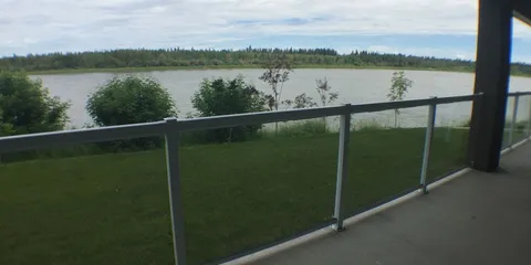 Balcony railing overlooking a lawn, trees and a river.