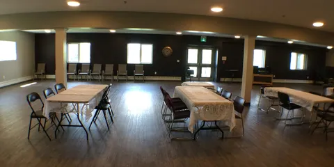 Gathering room with tables, folding chairs and wood-look flooring.