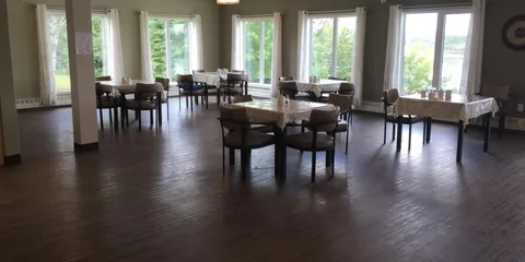 Dining room with tables, padded chairs and tall windows overlooking trees.