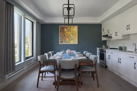 Dining table with upholstered chairs beside a kitchenette and windows