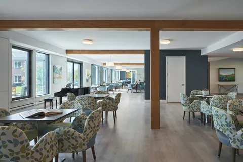 Room with patterned armchairs, tables and a piano beside windows