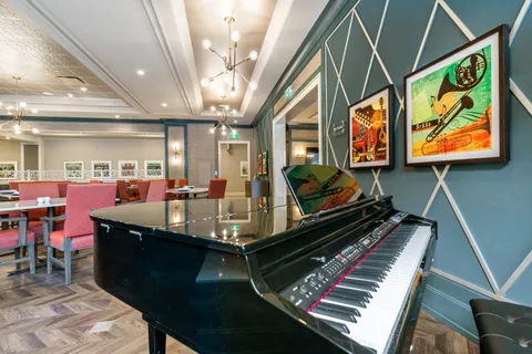 Dining room with red chairs and a grand piano beside framed musical instruments