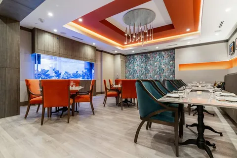 Dining table set with glasses beside an aquarium and orange chairs