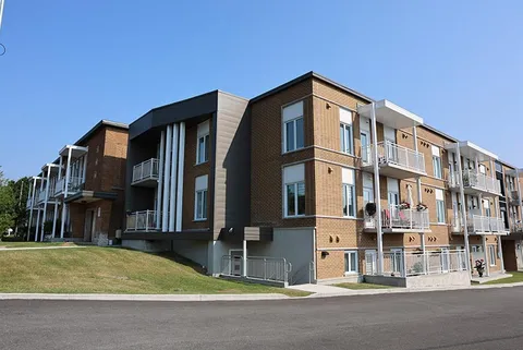 Brick building with balconies beside a driveway and sloping lawn