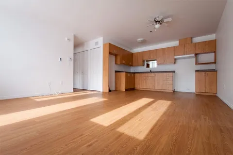 Empty room with wood flooring, wooden kitchen cabinets, a countertop and a ceiling fan
