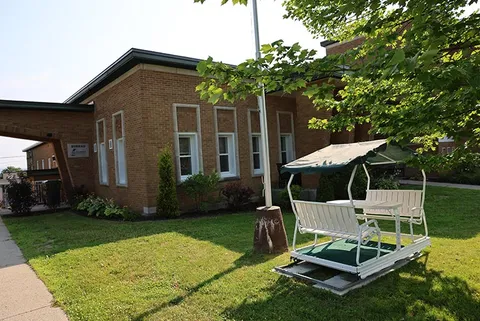 Covered white garden swing beside a brick building and trees