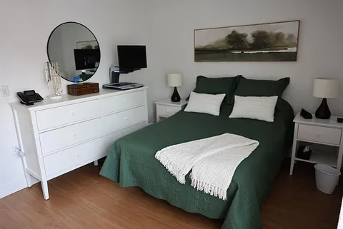 Bedroom with green bedding, white furniture and a round mirror