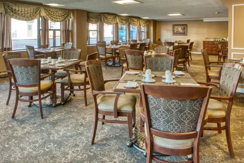 Dining room with set tables, upholstered chairs and large windows.