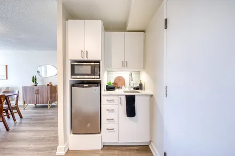 Kitchenette with white cabinets, sink, microwave and refrigerator.
