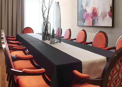 Long table with orange chairs, glass vases and abstract wall art