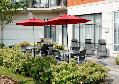 Courtyard with patio tables, red umbrellas, planted borders and a barbecue