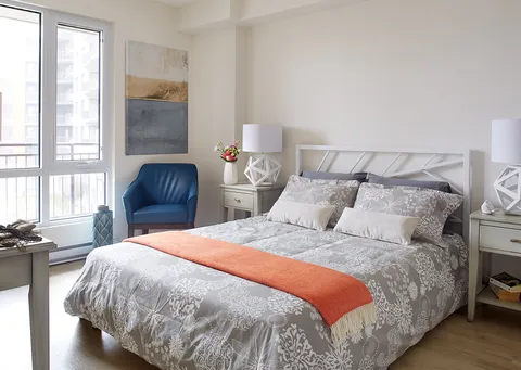 Bedroom with patterned white bedding, an orange blanket and a blue chair